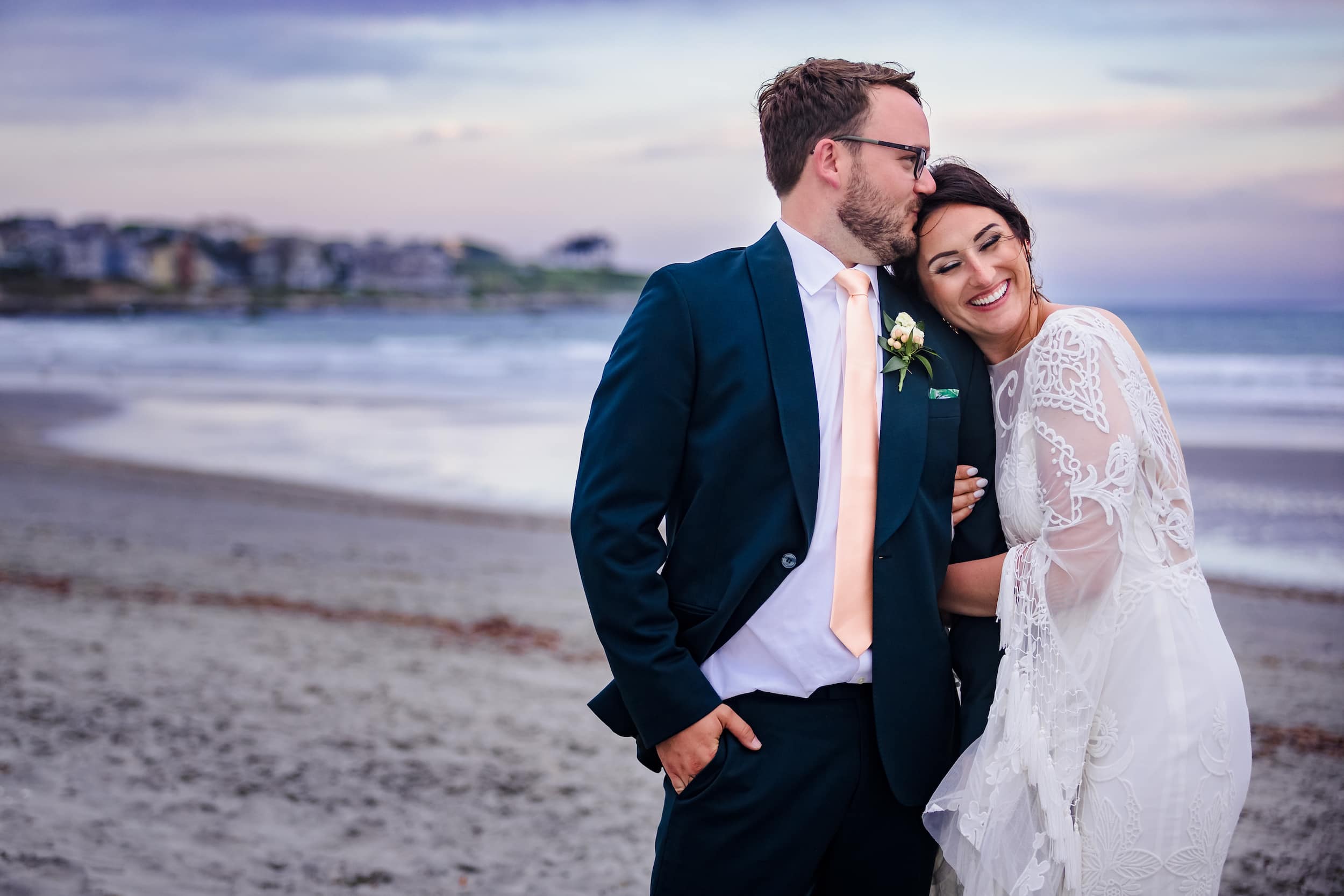 Groom kissing the bride’s forehead beside the beach in Newport, Rhode Island.