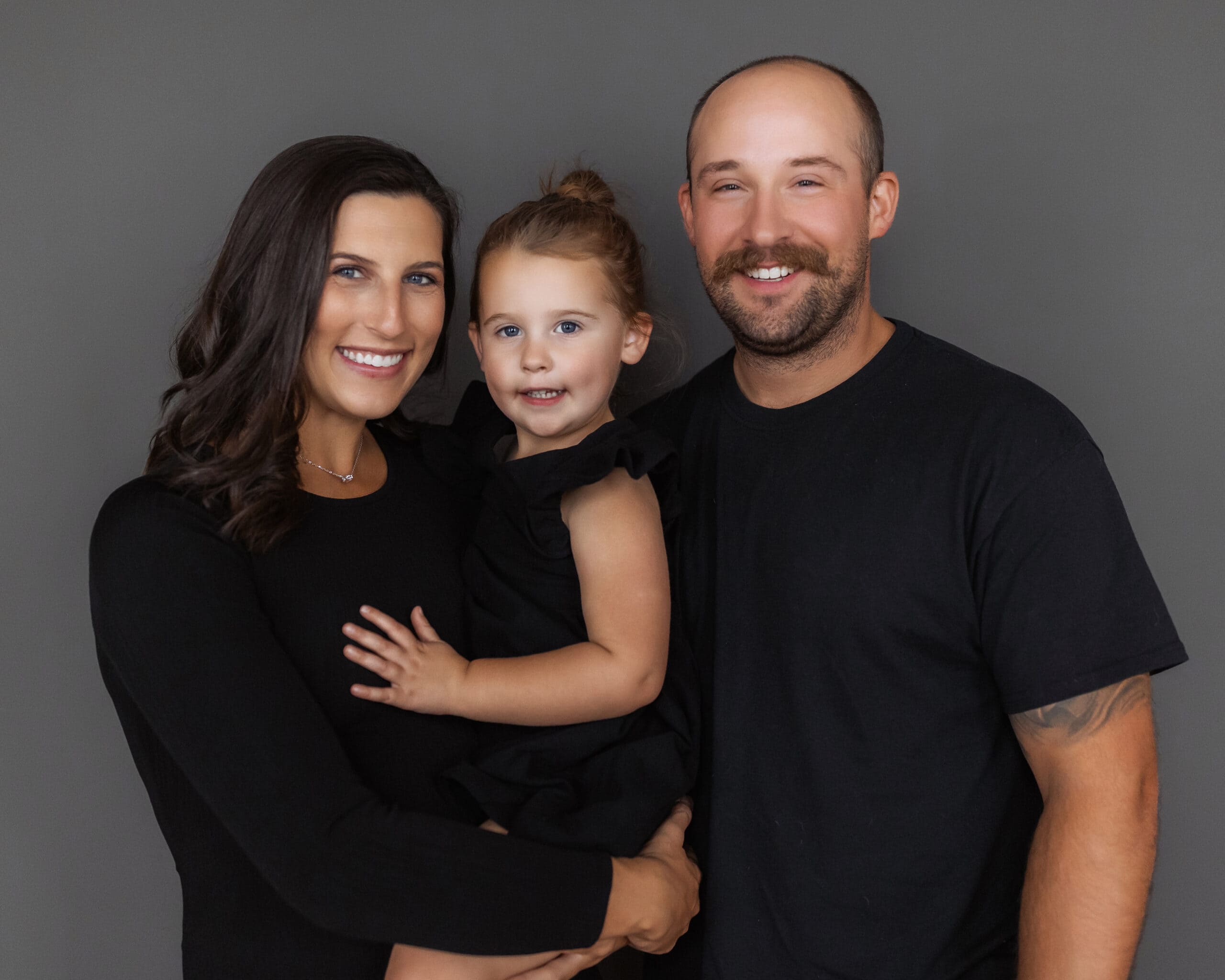 Happy family portrait featuring mother, father, and daughter smiling warmly together.