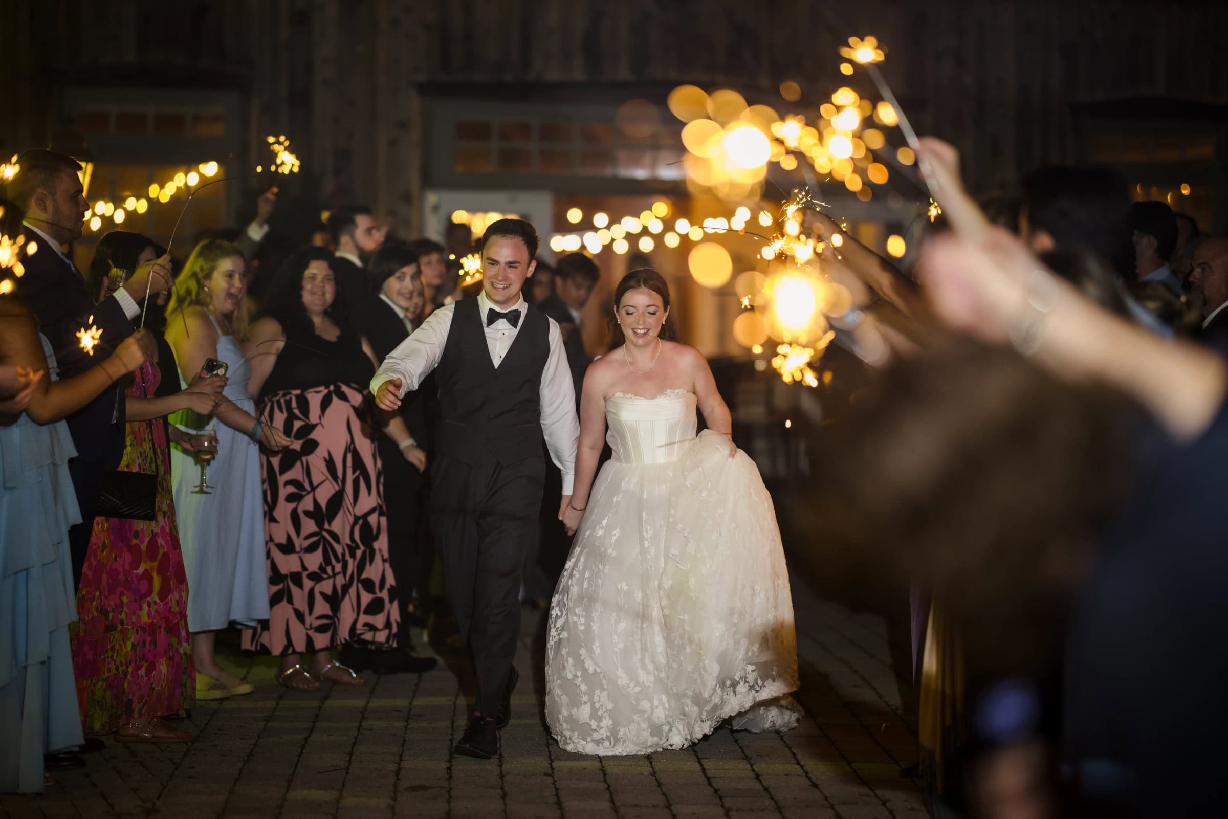 Bride and groom walk together down a paved aisle lined with guests holding sparklers at night. — Wedding at Glasbern Inn, Fogelsville, PA