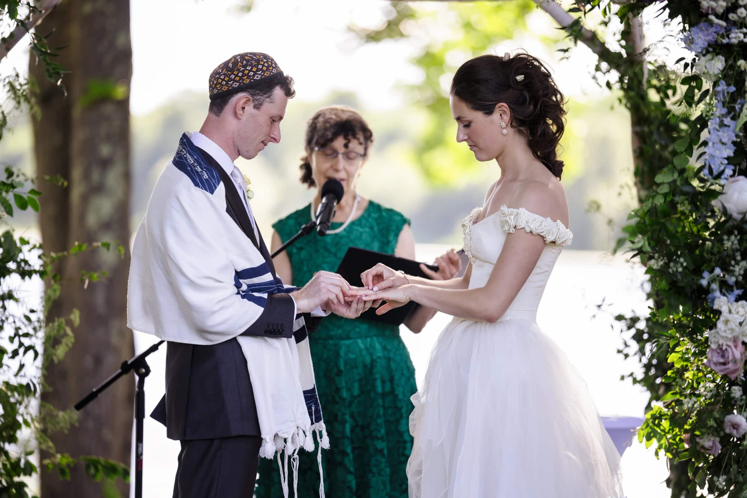 Bride and groom exchanging rings during their wedding ceremony while officiant holds the rings. — Wedding at Tyler Hill Camp, Tyler Hill, PA