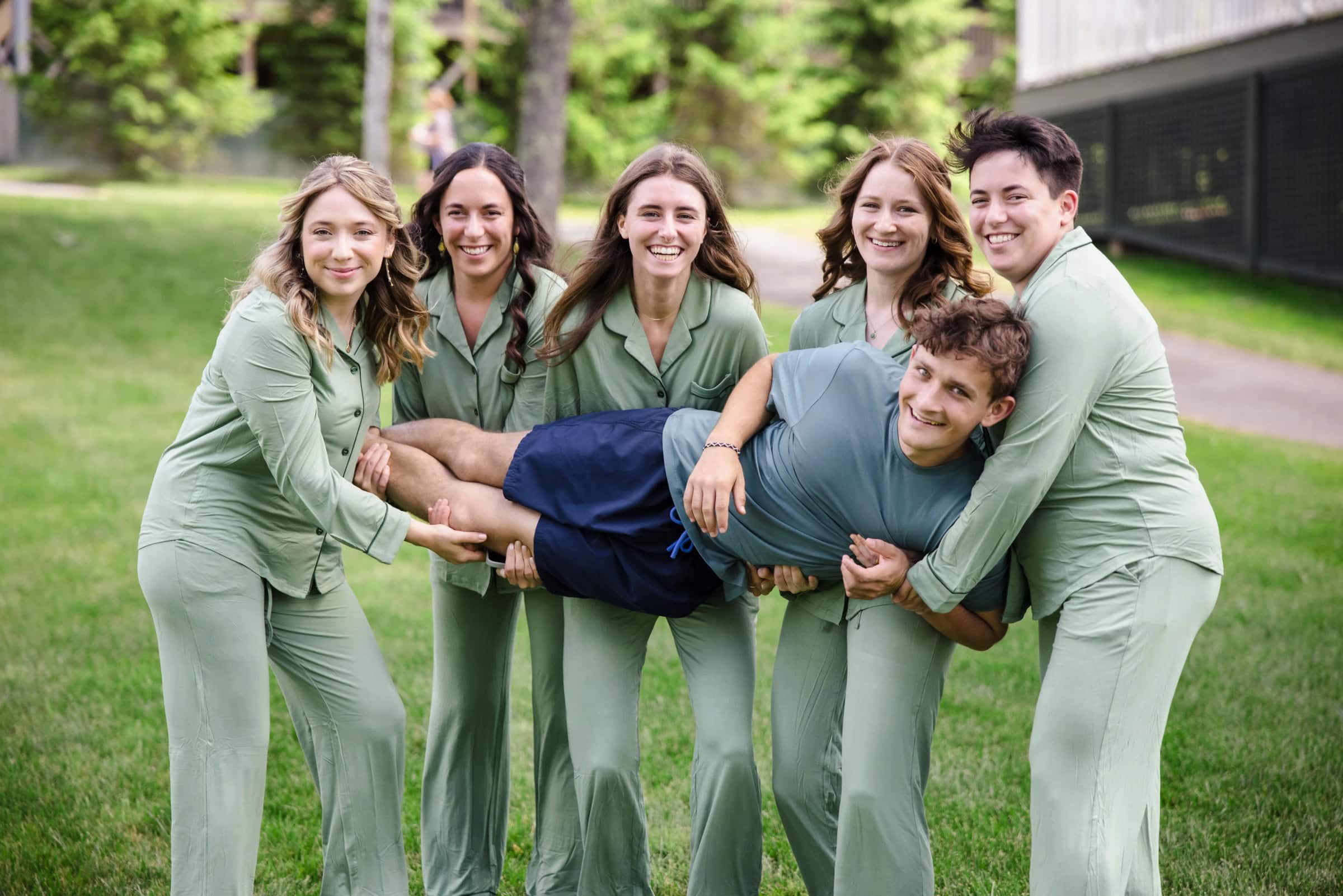 A group of young people lifting one person playfully in the air while posing together outdoors. — Wedding at Tyler Hill Camp, Tyler Hill, PA
