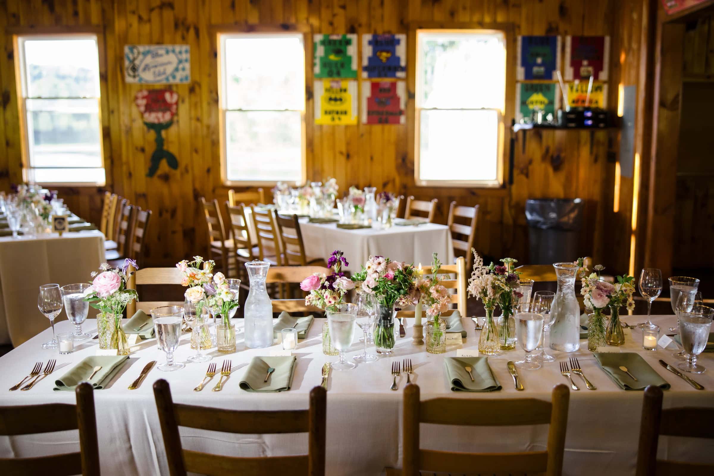 Long dining table set for a wedding reception, with floral centerpieces and place settings awaiting guests. — Wedding at Tyler Hill Camp, Tyler Hill, PA
