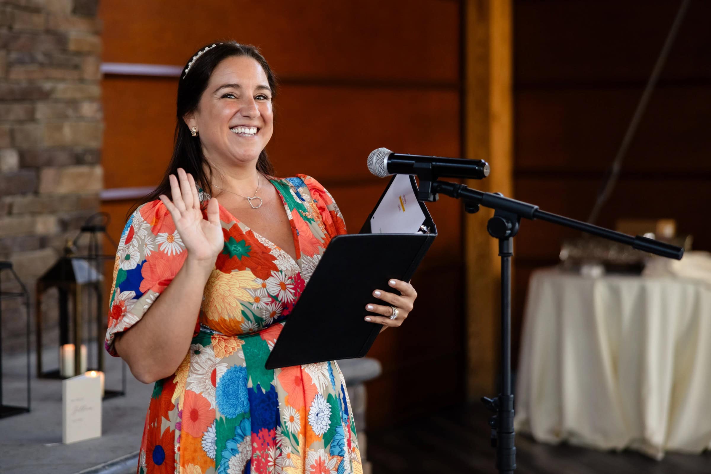 Woman speaking at a microphone while holding a tablet, gesturing expressively to an audience. &mdash; Wedding at Landmark Tavern at Stonehouse, Warren, NJ
