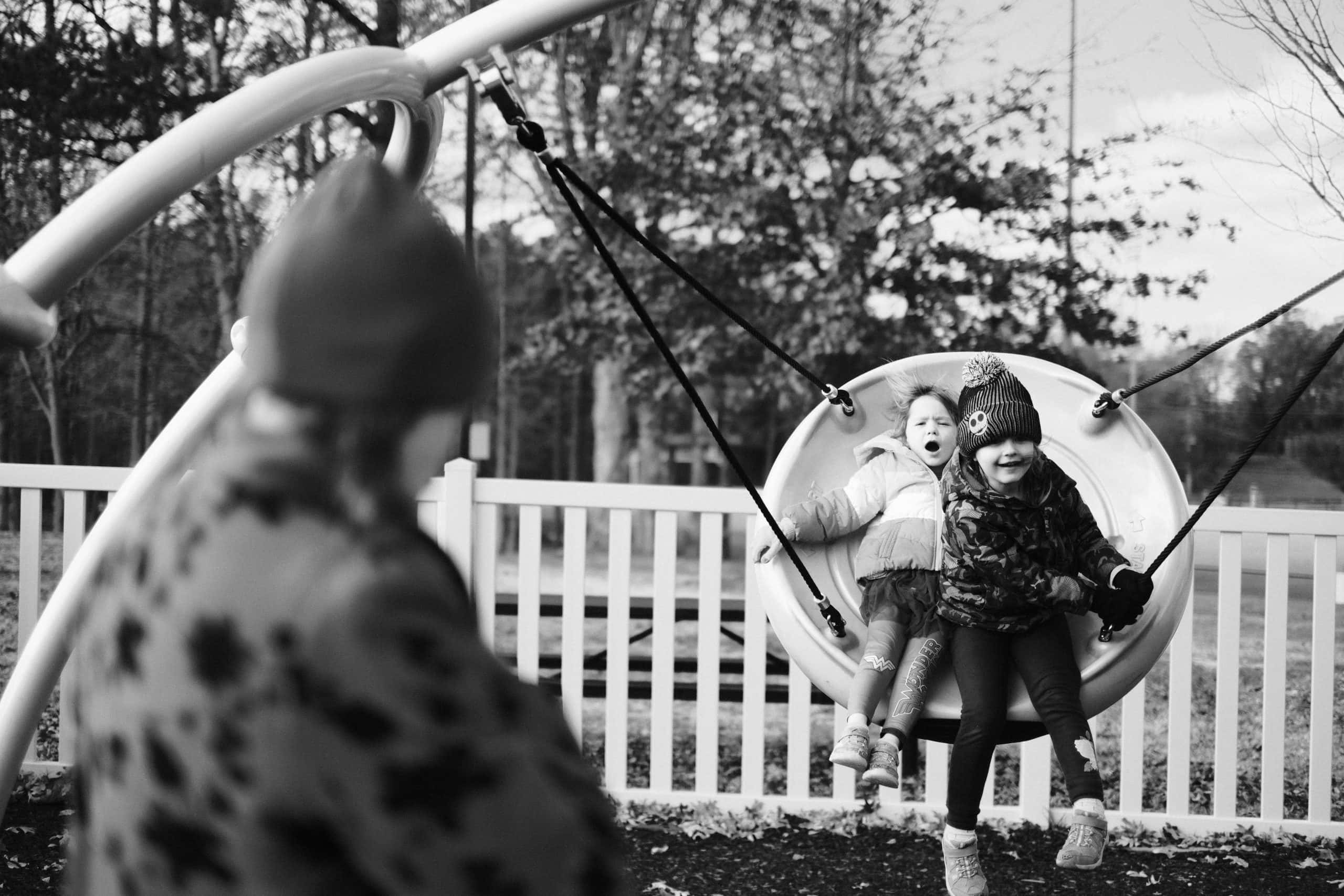 Children sharing a backyard swing while an adult pushes them.