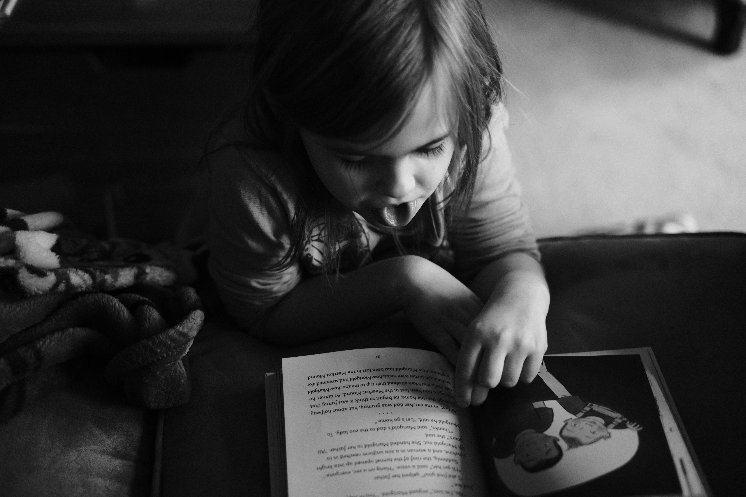 Black-and-white photograph of a child reading a book on the couch.
