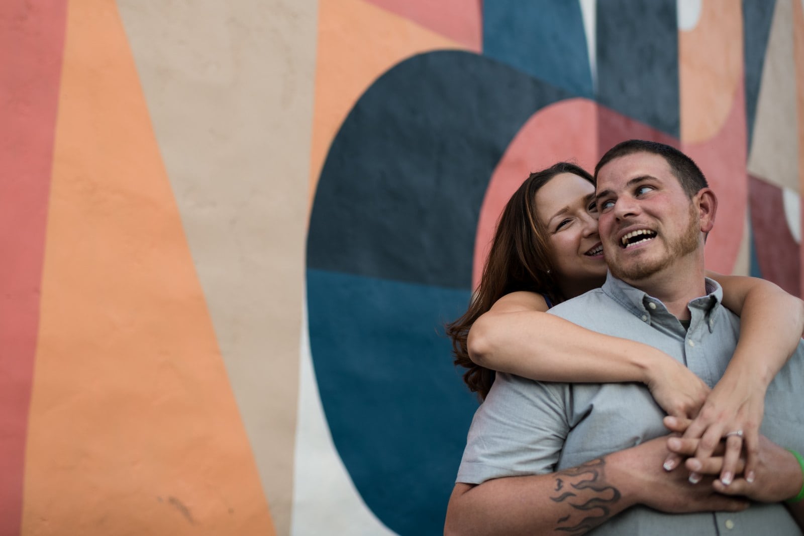 Woman hugging her laughing partner in front of a colorful geometric mural in Easton.