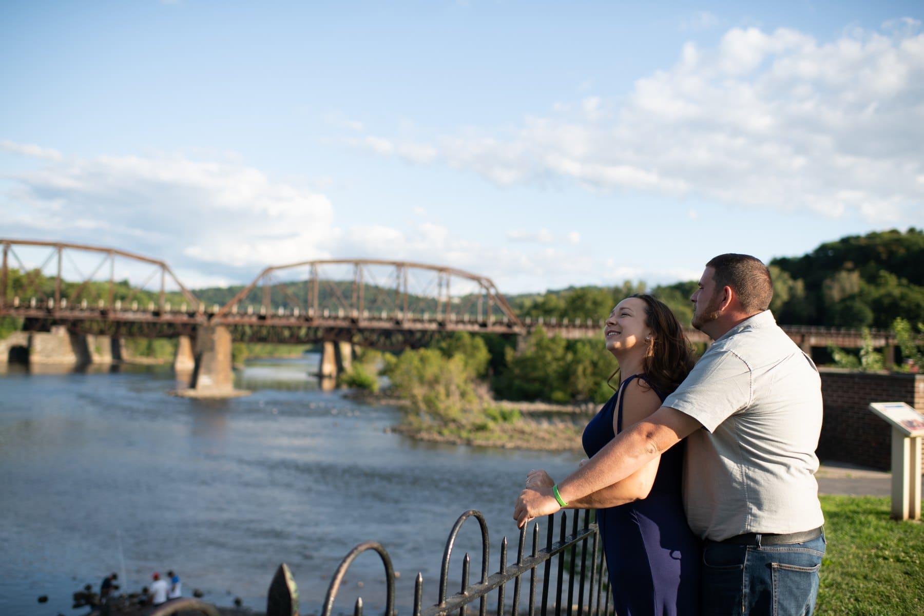 Couple leaning on a riverfront railing with an Easton bridge and the river behind them.