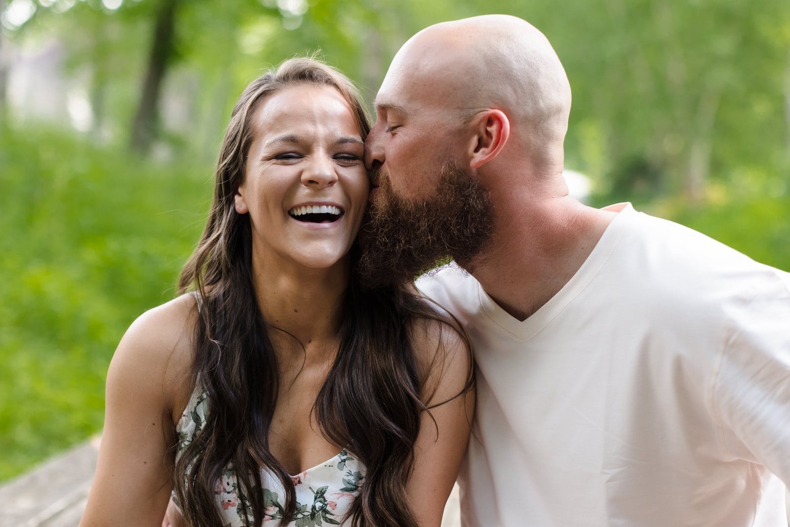 Woman laughing as her partner kisses her cheek outdoors.