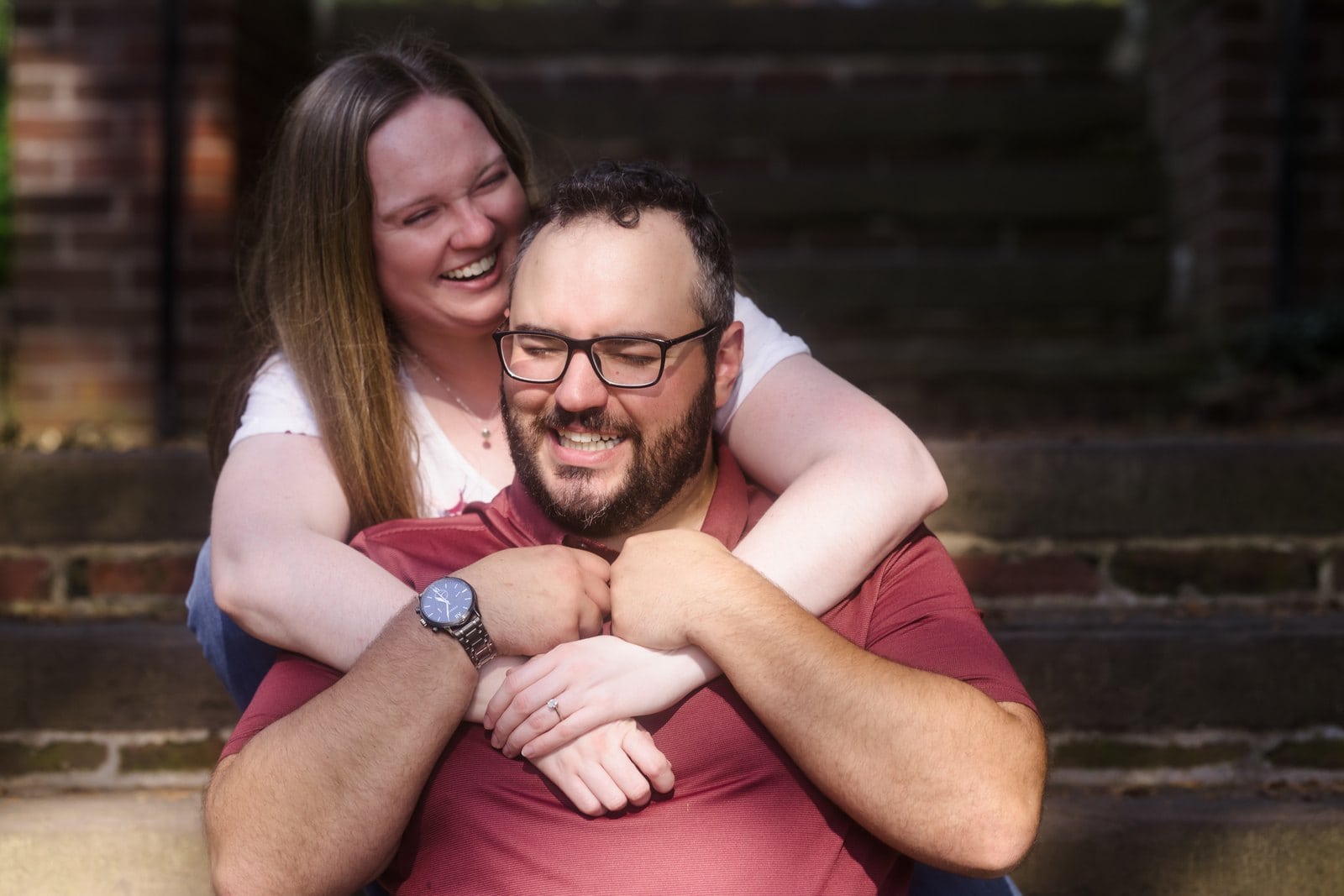 Woman laughing with her arms around her partner as they sit on brick steps.