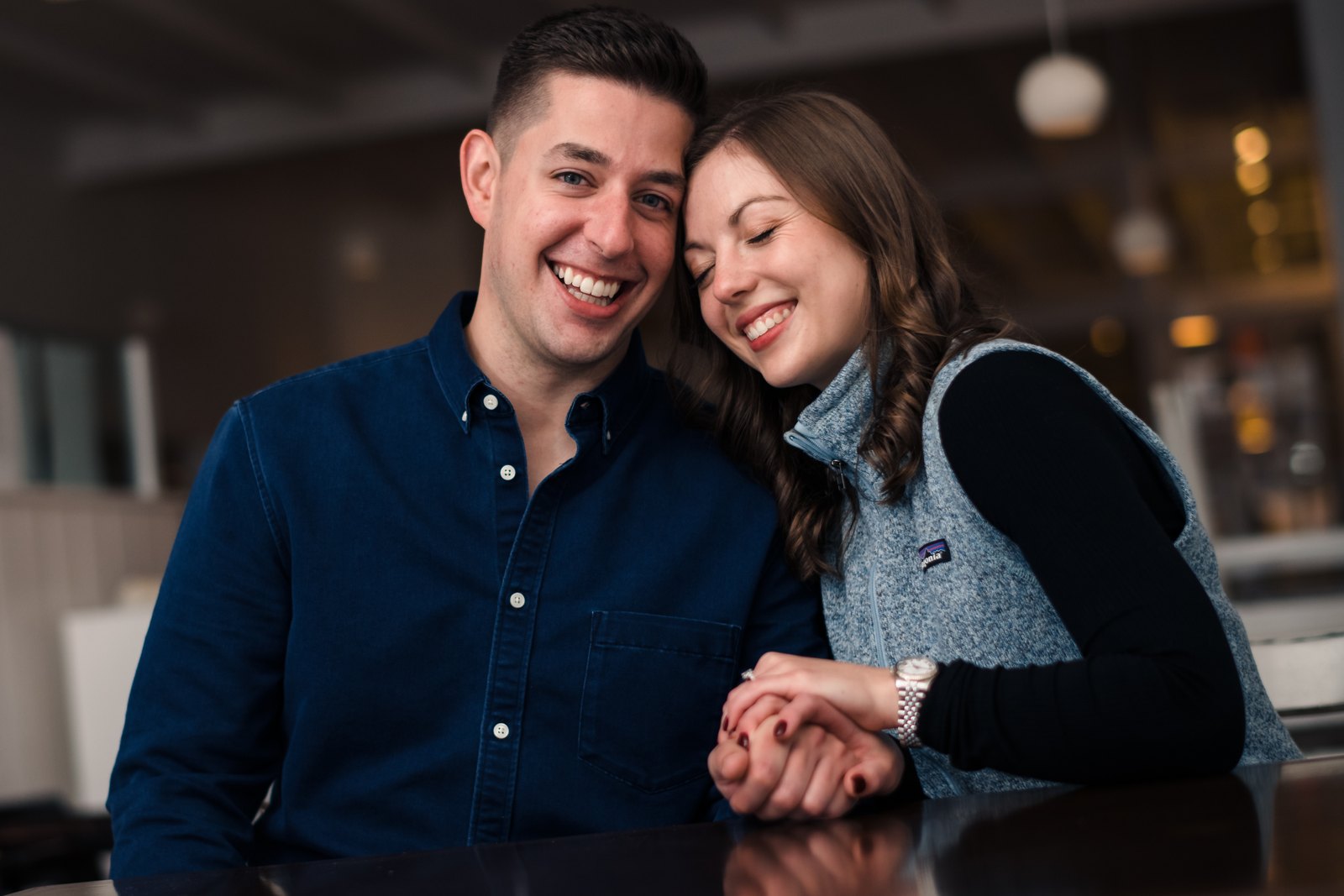 Couple leaning together and smiling while holding hands across a table.