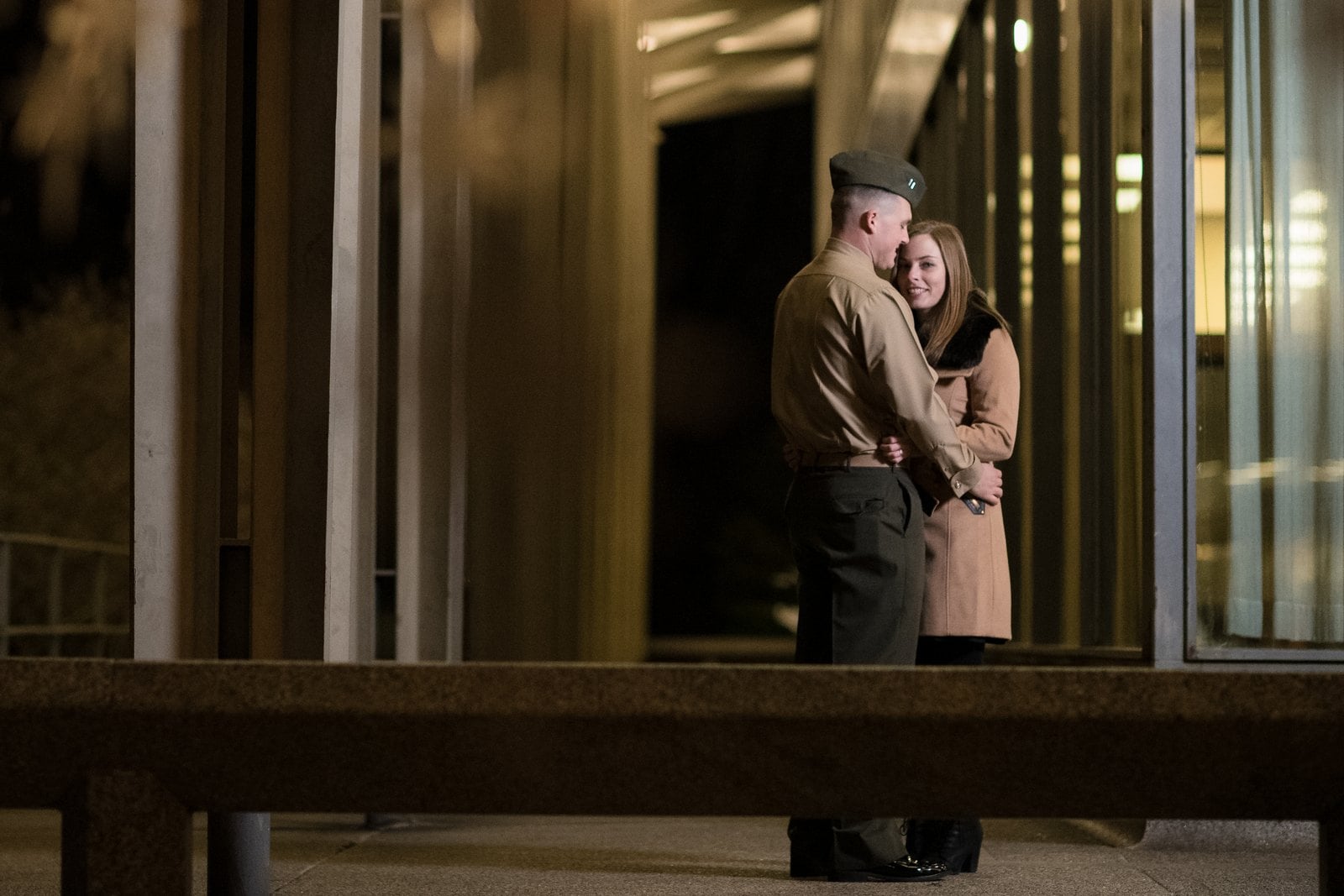 Couple embracing among repeating columns and windows in warm evening light.