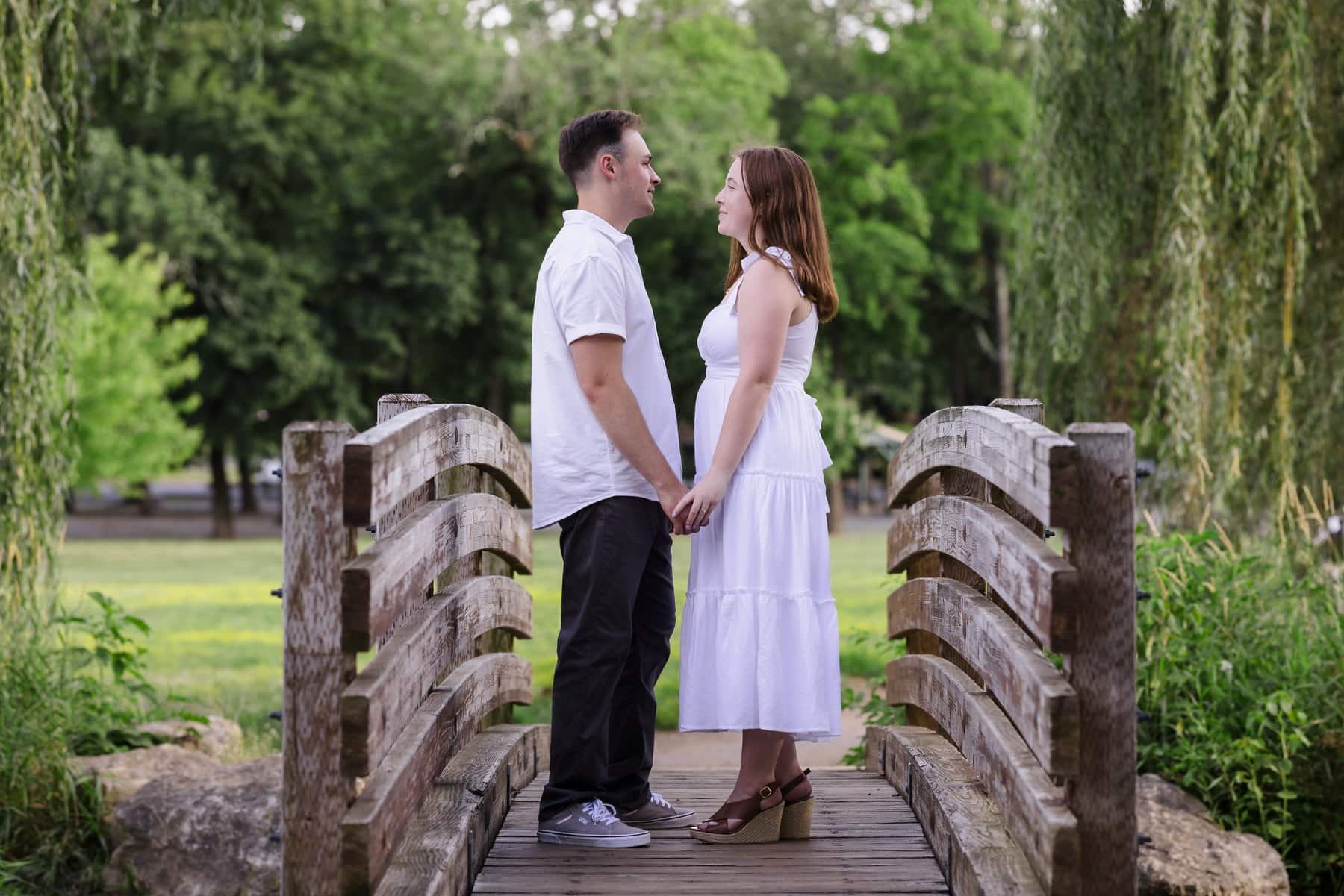 Couple holding hands on a wooden footbridge beneath willow branches in Lehigh Parkway.