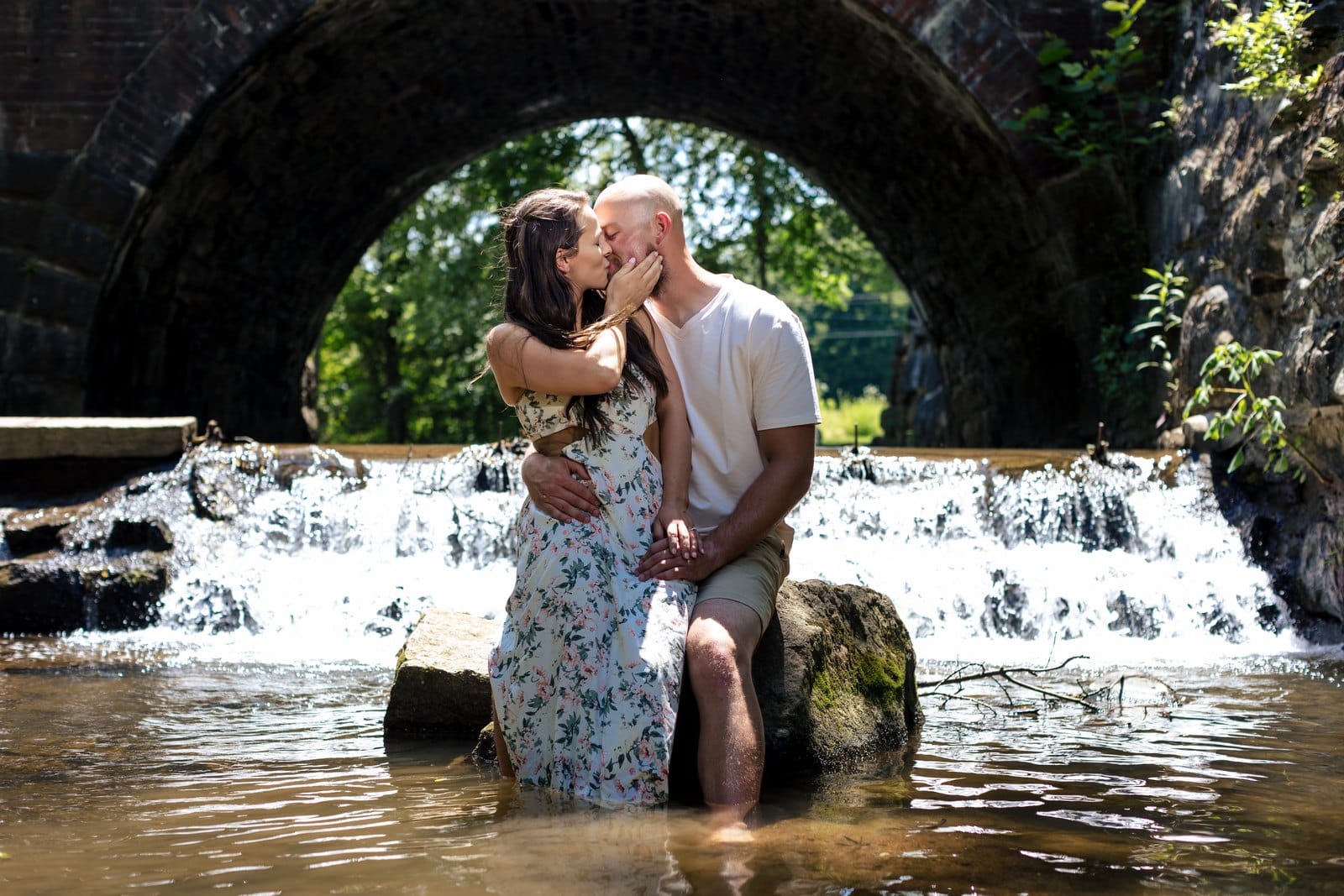 Couple kissing on a rock in the creek beneath a stone arch at Lockridge Park.