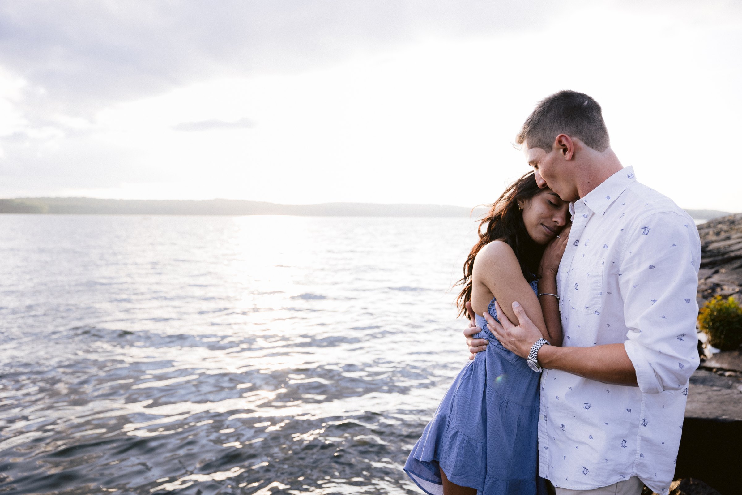 Man kissing his partner on the forehead beside the sunlit waters of Lake Wallenpaupack.