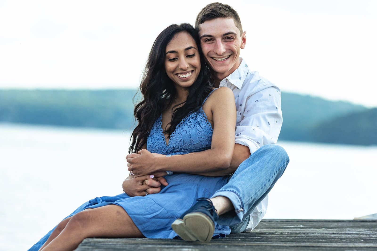 Couple sitting close together on a wooden dock with Lake Wallenpaupack behind them.
